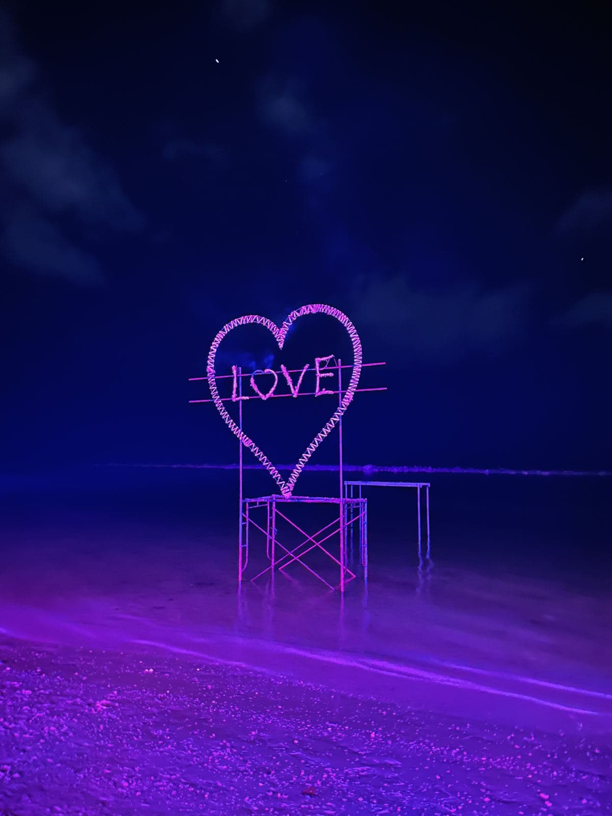 A neon LOVE sign glowing on the beach at night